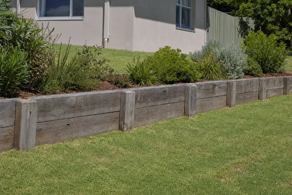 A finished timber sleeper retaining wall along a sloping backyard, with a garden bed planted above it — timber sleeper retaining wall, Gosford and the Central Coast. Illustrative example.